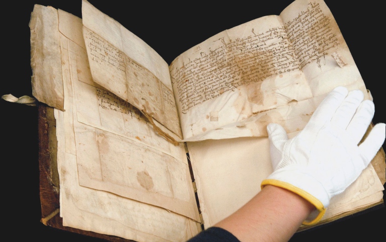 En hand med vit handske på bläddrar i en väldigt gammal bok.