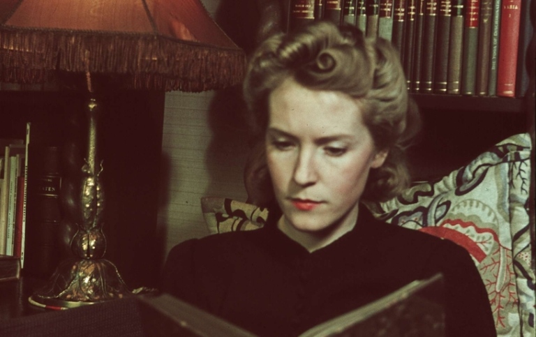 En kvinna sitter och läser en bok vid en lampa. 